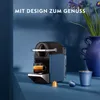 A Nespresso coffee machine with a cup of coffee and coffee capsules, set against a blue background with a vase and flowers. Produktbild-Vorschau
