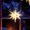 A lit-up star-shaped lantern hanging in front of a window with a blurred background of blue and orange hues, suggesting a nighttime or festive scene. Produktbild-Vorschau