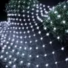 A net of white LED lights is draped over bushes and the ground at night. Produktbild-Vorschau