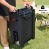 A person is holding a large black beverage dispenser outdoors, with camping chairs and a table in the background. Anteprima dell’immagine prodotto