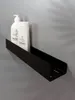 A black shelf mounted on a gray wall with two white bottles of soap or lotion on it. Produktbild-Vorschau