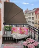 A cozy balcony setup with a brown awning, wooden crate seating, colorful cushions, and plants. Produktbild-Vorschau