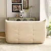 A beige sofa is placed in a living room setting, with artwork and a cabinet in the background. Produktbild-Vorschau