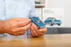 A person's hands are holding a blue model car, with a box featuring a similar car in the background. Náhľad obrázku produktu