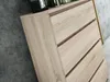 A close-up view of a wooden chest of drawers with visible wood grain. Produktbild-Vorschau