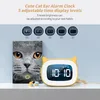 A yellow cat-ear alarm clock is displayed next to a book titled 'The Cat Book'. The background features text and circular graphics illustrating different brightness levels. Produktbild-Vorschau