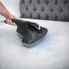 A hand is holding a black and gray handheld vacuum cleaner over a white mattress. Produktbild-Vorschau