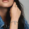 A close-up shot of a woman's wrist wearing a Pandora bracelet with a heart-shaped charm. Podgląd zdjęcia produktu