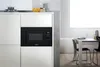 A built-in microwave oven integrated into a kitchen cabinet, with a dining table and chairs visible in the background. Voir les images du produit