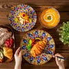 A top-down view of a table setting with a colorful bohemian-style dinnerware set, featuring plates of food and a bowl of soup. Náhled obrázku produktu