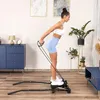 A woman is using a stepper machine with resistance bands in a living room. Voir les images du produit