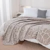 A close-up view of a beige blanket with a leaf pattern draped over a bed. Podgląd zdjęcia produktu