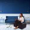 A woman is working on her laptop while sitting on a folded mattress in a modern living room. Voir les images du produit