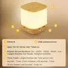 A close-up of a modern LED table lamp with wood accents, featuring instructional callouts and text descriptions. Produktbild-Vorschau