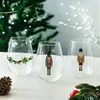 Three stemless wine glasses with Christmas-themed designs are displayed on a table with a Christmas tree in the background. Produktbild-Vorschau