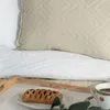 A close-up view of a bed with a white quilted blanket and a beige pillow, with a breakfast tray holding a pastry and coffee cup in the foreground. Náhľad obrázku produktu