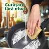 A hand is cleaning a black frying pan under running water in a kitchen sink. Produktbild-Vorschau