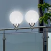 Two white globe lights are attached to a metal railing on a balcony. Náhled obrázku produktu
