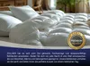 A close-up view of a fluffy white duvet on a bed, with pillows in the background. Produktbild-Vorschau
