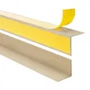 A close-up, angled view of two beige corner profiles, one with yellow double-sided tape being peeled off. Produktbild-Vorschau