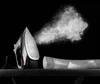 A steam iron is shown emitting steam, with a folded white shirt on an ironing board. Produktbild-Vorschau