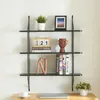 A black metal wall shelf with various decorative items and books displayed on it, placed above a desk. Produktbild-Vorschau