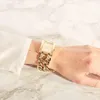 A person's wrist wearing a gold watch with a chain-link band, against a marble background. Náhled obrázku produktu