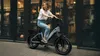 A woman is riding an electric bicycle on a city street. Produktbild-Vorschau