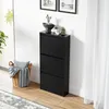 A black shoe cabinet with three flip-down doors stands against a white wall, next to a basket filled with blankets and a pillow. Náhľad obrázku produktu