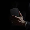 A person in a suit holds a black smartphone case with a camera cover. Náhled obrázku produktu