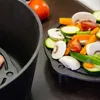A close-up view of a cast iron grate with various chopped vegetables and mushrooms, next to a black cast iron pot. Produktbild-Vorschau