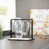 A black drying rack holding two baby bottles and a baby bottle warmer, with a cookbook in the background. Náhled obrázku produktu