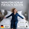 A woman in pajamas is happily sitting on a bed with a white duvet. Produktbild-Vorschau