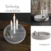 A collage of images showcasing a round, light gray candle holder with multiple candle slots, some with lit candles and a small sprig of greenery. Produktbild-Vorschau