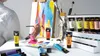 An artist is painting on a canvas with acrylic paints, surrounded by tubes of paint and brushes. Anteprima dell’immagine prodotto