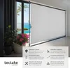 A white roller blind is shown extended in front of a large glass door overlooking a tropical scene with a pool and ocean. Plants are in pots to the left of the blind. A section of the image contains text and icons describing the product's features. Náhled obrázku produktu