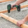 A person is using a cordless drill to drill a hole in a wooden beam, with gravel and other wooden beams in the background. Náhled obrázku produktu