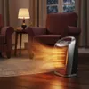 A ceramic heater is shown in a cozy living room setting, emitting warm air. Podgląd zdjęcia produktu