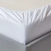 A close-up view of a white fitted sheet with elastic gathering at the edge, draped over a grey bed base. Produktbild-Vorschau