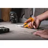 A person is using orange scissors to cut fabric or paper patterns on a table. Podgląd zdjęcia produktu