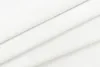 A close-up view of white fabric, folded to create diagonal lines and shadows. Produktbild-Vorschau