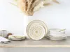 A set of white and gold mandala-patterned plates and bowls are arranged on a wooden shelf, with a vase of dried pampas grass in the background. Náhľad obrázku produktu