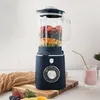 A navy blue stand mixer filled with fruit sits on a wooden cutting board next to a glass of pink smoothie. Produktbild-Vorschau