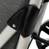 A close-up of a black plastic component attached to a silver metal frame, with a gray fabric background and a black wheel visible in the background. Náhled obrázku produktu