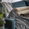 Several soft blankets are neatly folded and draped on a teal sofa, with a plant in the foreground. Produktbild-Vorschau