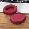 Two red ear pads for headphones are placed on a wooden surface next to a laptop keyboard. Podgląd zdjęcia produktu