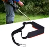 A person is using a string trimmer in a grassy area, with a close-up of the trimmer's shoulder strap in the foreground. Náhled obrázku produktu
