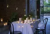 An outdoor table setting at dusk, decorated with string lights and candles. Náhled obrázku produktu