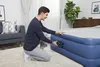 A man is kneeling and using an electric pump to inflate an air mattress in a living room. Produktbild-Vorschau