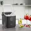 A black ice maker is shown on a kitchen counter next to two glasses of red cocktails and a glass of a clear drink with lime and mint. There are also some raspberries and lime slices scattered on the counter. Podgląd zdjęcia produktu